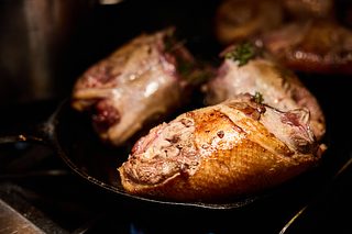Golden-brown roasted poultry pieces searing in a cast-iron skillet, with the rest of the pan fading into shadow.